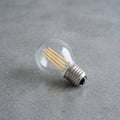 Ampoule LED à filament E27 G45 allongée sur béton gris, filaments dorés, culot nickel