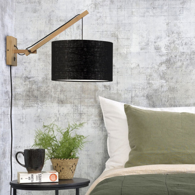 Applique murale Andes en bambou et abat-jour en lin noir installée au-dessus d'une table de chevet dans une chambre