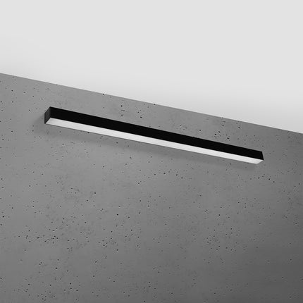 Applique barre moderne LED noire 118 cm installée sur un mur de béton