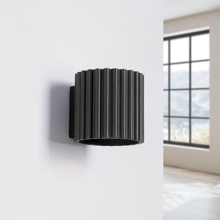 Applique cannelée Aura noire fixée au mur d'une chambre épurée près d'une fenêtre