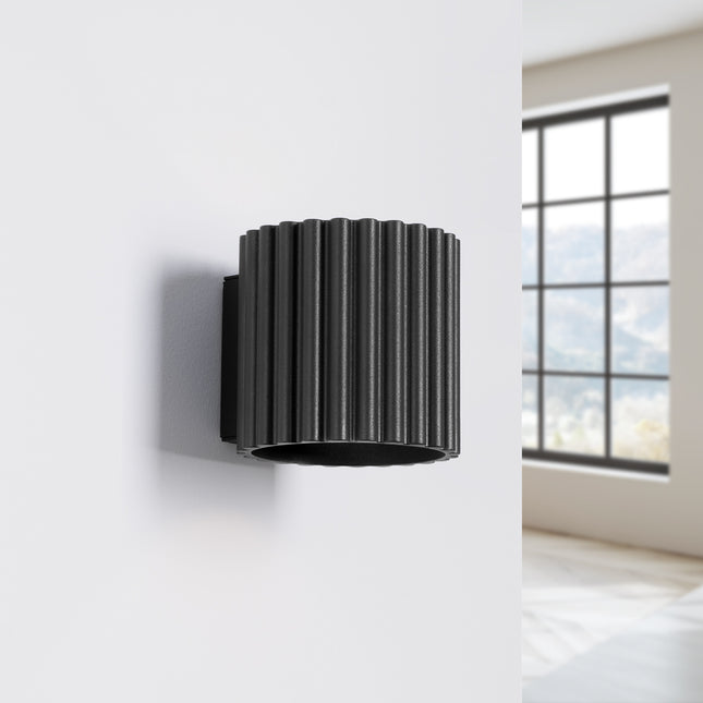 Applique cannelée Aura noire fixée au mur d'une chambre épurée près d'une fenêtre