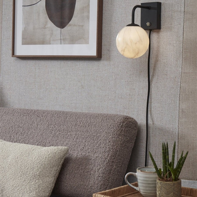 Applique murale Carrara globe en verre effet marbre blanc et bras noir mat, allumée près d'un canapé