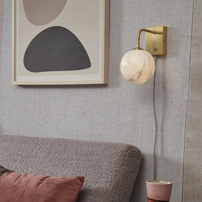 Applique murale Carrara globe en verre effet marbre blanc et bras doré, allumée dans un salon