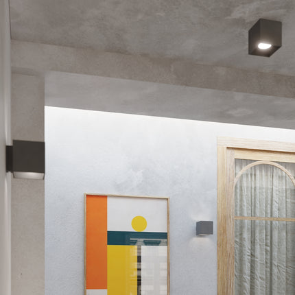 Détail rapproché d'une applique cube anthracite allumée au mur