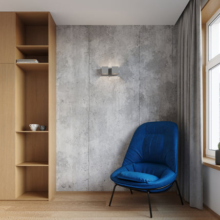 Applique Cube LED 2 feux allumée sur mur béton, ambiance chaleureuse près d'un fauteuil bleu