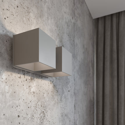 Gros plan de l'applique Cube LED 2 feux grise allumée, lumière rasante sur mur en béton