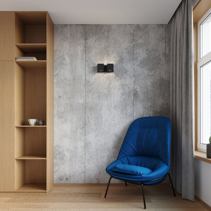 Applique Cube LED 2 feux allumée sur mur béton, ambiance chaleureuse près d'un fauteuil bleu