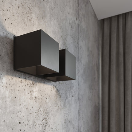 Gros plan de l'applique Cube LED 2 feux noire allumée, lumière rasante sur mur en béton