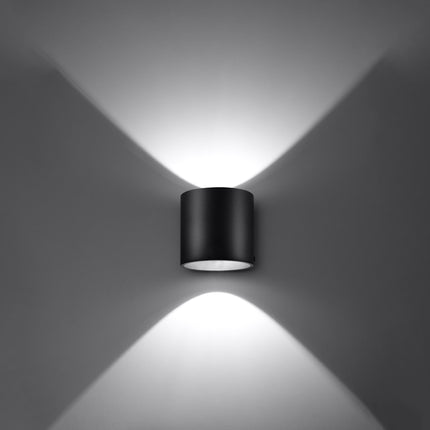 Applique cylindrique noire projetant un faisceau de lumière net sur un mur