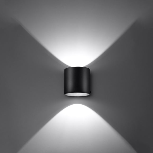 Applique cylindrique noire projetant un faisceau de lumière net sur un mur