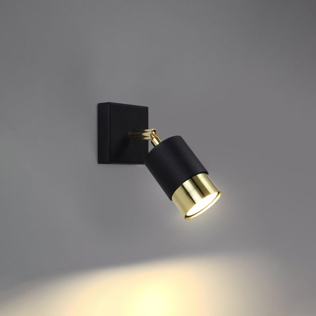 Applique Double Cylindre noir et doré allumée, faisceau dirigé sur un mur gris