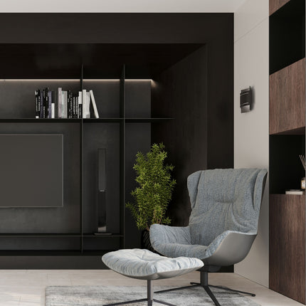 Applique Double Rampe noire installée au mur d'un salon sombre, près d'un fauteuil design gris.