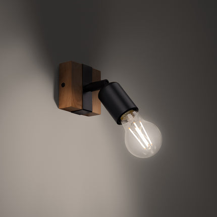 Applique Élégance Bois Noir allumée sur un mur sombre, lumière chaude diffusée par l'ampoule à filament