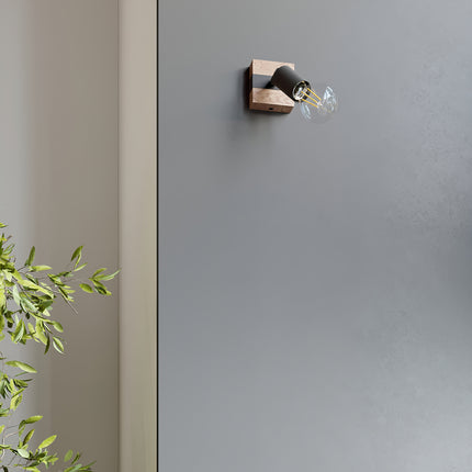 Applique Élégance Bois Noir installée sur un mur gris foncé, ambiance épurée avec une plante verte