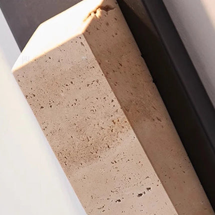 Applique extérieure en pierre naturelle noire éclairant une terrasse aménagée avec fauteuil