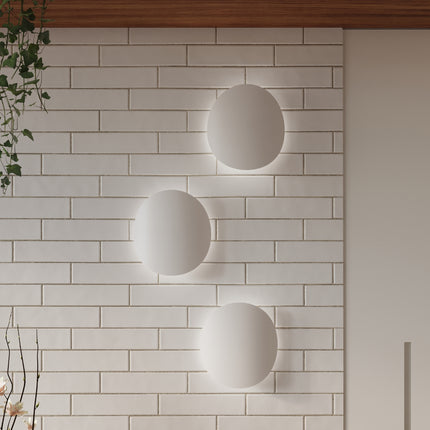 Composition de trois appliques galet Ombre Douce blanches, halos de lumière sur mur clair
