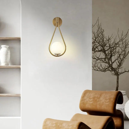Applique murale goutte dorée au globe de verre opale dans un salon avec fauteuil cuir