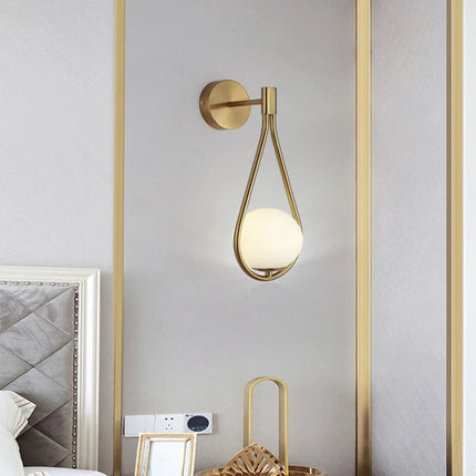 Applique murale goutte dorée à globe de verre opale au-dessus d'une tête de lit capitonnée