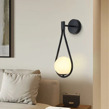 Applique murale goutte noire au globe de verre opale près d'un canapé beige