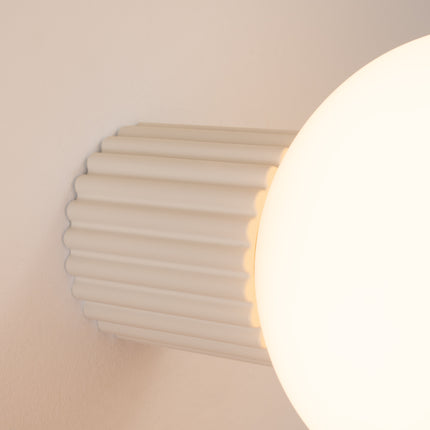 Gros plan sur les nervures du socle aluminium beige et le globe en verre de l'applique Halo