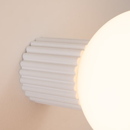 Gros plan sur les nervures du socle aluminium blanche et le globe en verre de l'applique Halo