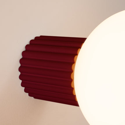 Gros plan sur les nervures du socle aluminium bordeaux et le globe en verre de l'applique Halo