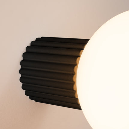 Gros plan sur les nervures du socle aluminium noire et le globe en verre de l'applique Halo