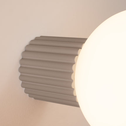 Gros plan sur les nervures du socle aluminium taupe et le globe en verre de l'applique Halo