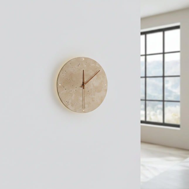 Applique horloge en travertin allumée sur un mur clair, halo lumineux chaud diffusé autour du disque