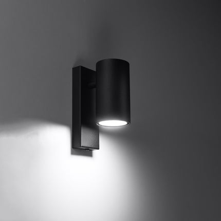 Applique murale noire allumée projetant un halo de lumière douce vers le bas sur le mur