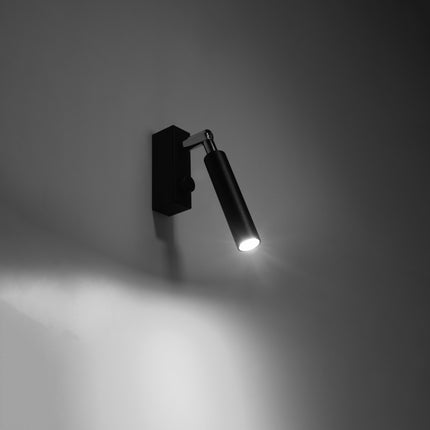 Applique liseuse acier noir allumee dans une ambiance tamisee, faisceau precis sur le mur