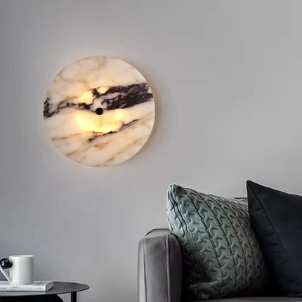 Applique en marbre naturel diffusant une lumière chaude au dessus d'un canapé gris et de coussins