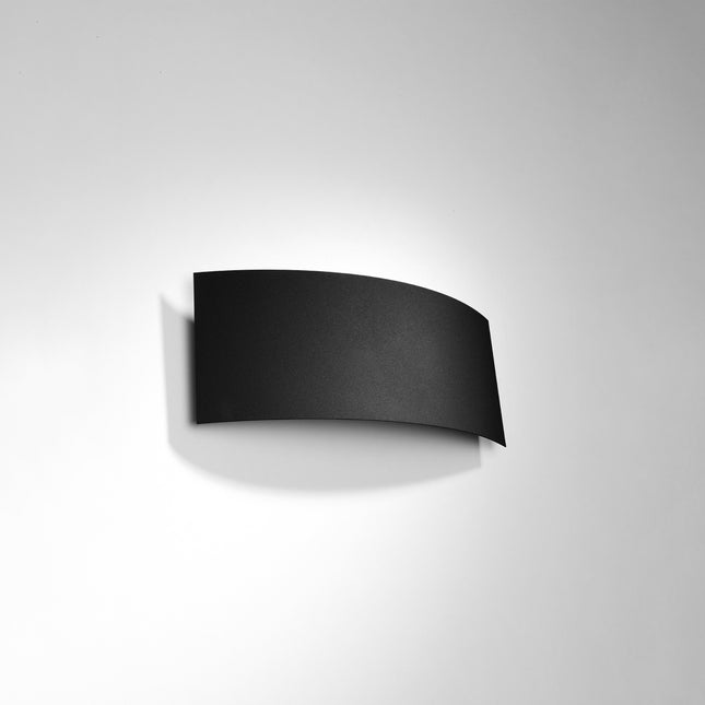 Applique murale Arc noire vue de face, lame d'acier courbée contre un mur gris clair