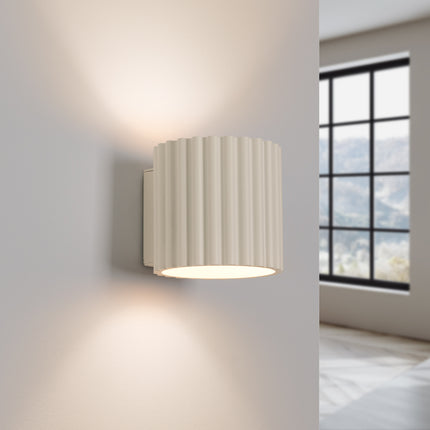 Applique Aura beige allumée, éclairage bi-directionnel haut et bas sur un mur clair