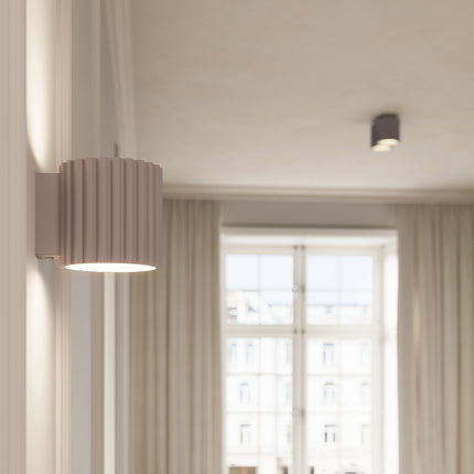 Applique murale Aura taupe allumée près d'une fenetre, lumiere chaleureuse
