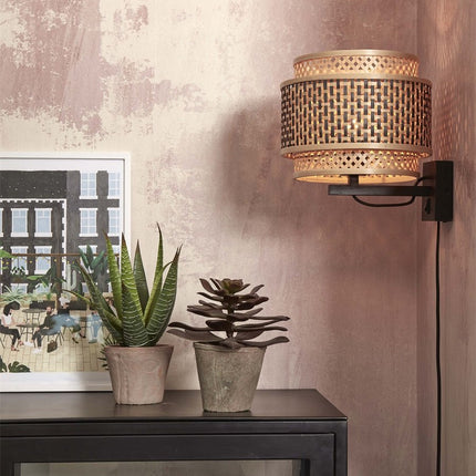 Applique murale Bhutan en bambou tressé noir et naturel, fixée au mur au-dessus d'un meuble avec plantes vertes
