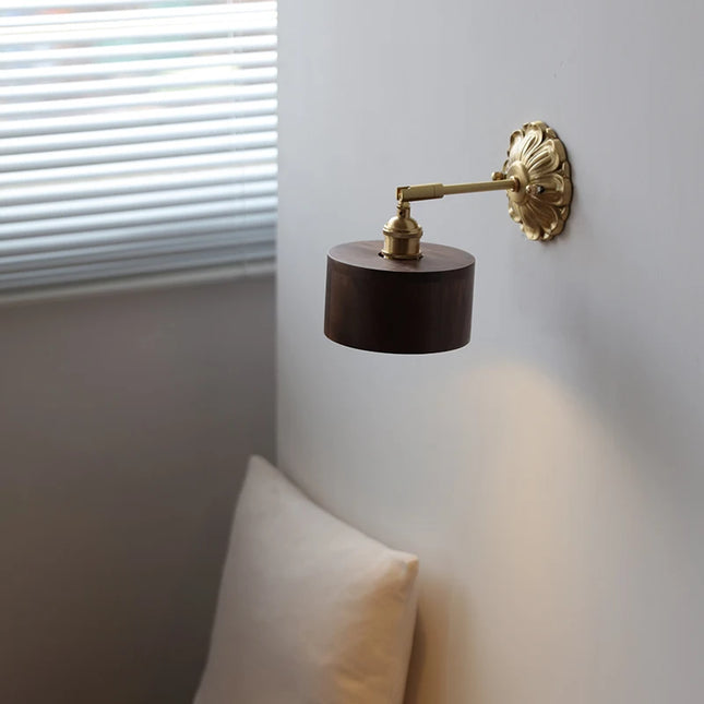 Applique murale bois foncé et laiton allumée près d une fenêtre au-dessus d un coussin dans une chambre
