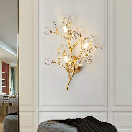 Applique murale branches en cristal et métal doré allumée sur un mur à moulures dans un salon élégant
