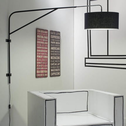 Vue d'ensemble de l'applique Brighton, large abat-jour en coton noir diffusant une lumière douce au-dessus d'un fauteuil