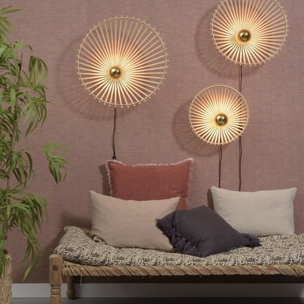Trois appliques murales en bambou tressé de tailles variées, disposées sur un mur rose au-dessus d'une banquette