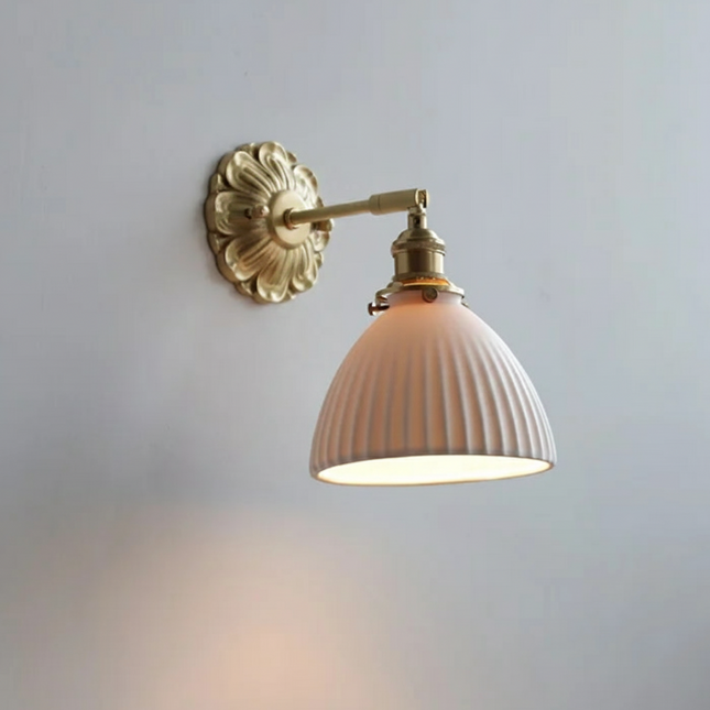 Applique murale en céramique rosé cannelée et laiton doré fixée sur un mur clair, diffusant une lumière chaude et tamisée