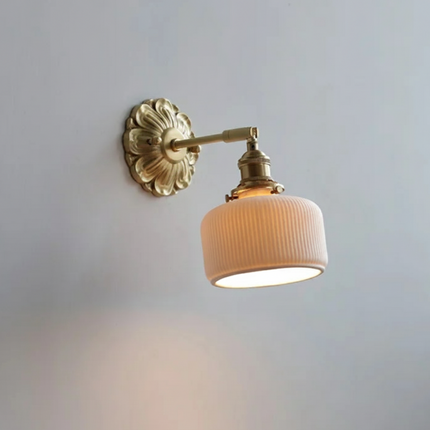 Applique murale en céramique cannelée crème et laiton doré, bras orientable, allumée sur un mur clair