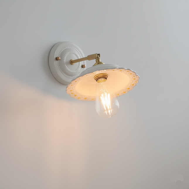 Applique murale en céramique blanche festonnée et bras en cuivre, allumée d'une lumière chaude sur un mur clair