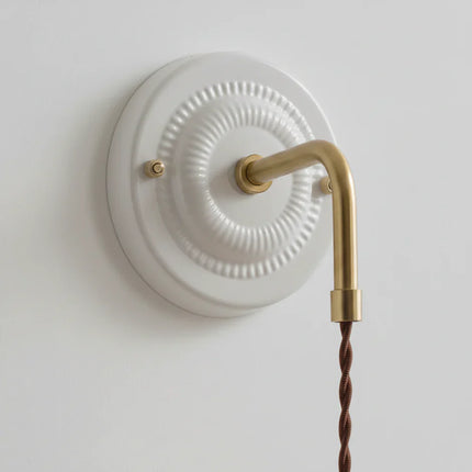 Détail de la platine ronde en céramique striée et du bras orientable en laiton doré de l'applique murale