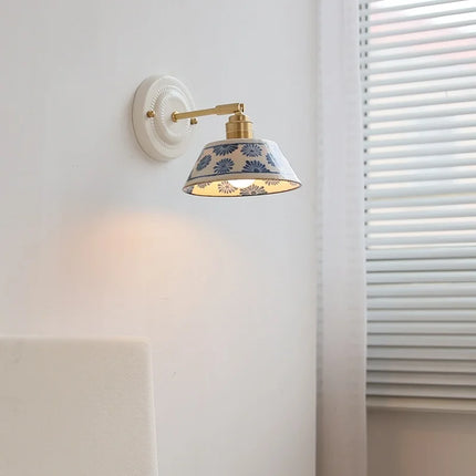Applique murale en céramique à motif floral bleu et bras cuivre allumée sur un mur clair dans une chambre