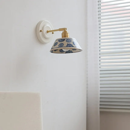 Applique murale en céramique à motif floral bleu et monture cuivre éteinte, près d'une fenêtre à stores
