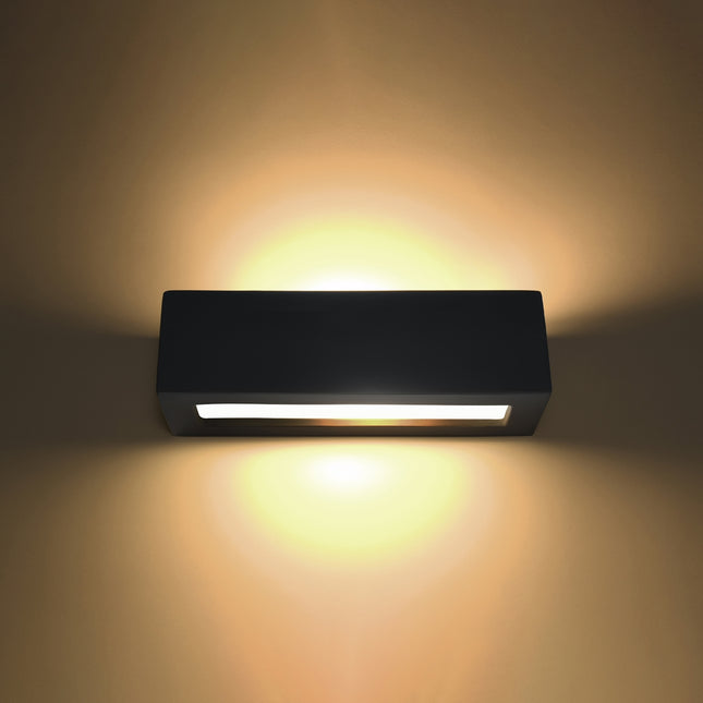 Applique murale céramique noire allumée diffusant une lumière chaude vers le haut et le bas