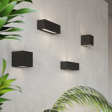 Appliques murales céramique noire allumées sur un mur béton avec plantes vertes