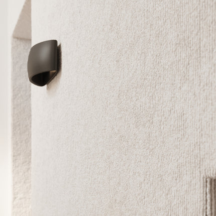 Détail de l'applique Coquille en céramique noire posée sur un mur texturé beige