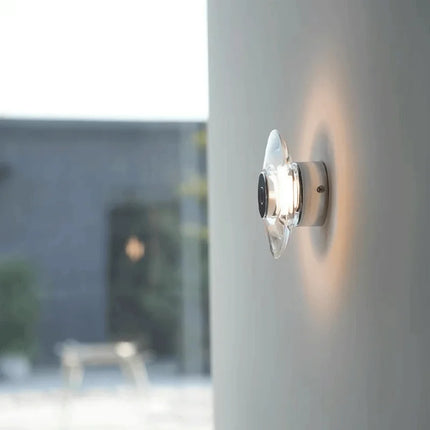 Applique murale LED en cristal allumée sur un mur clair, halo de lumière chaude autour du disque
